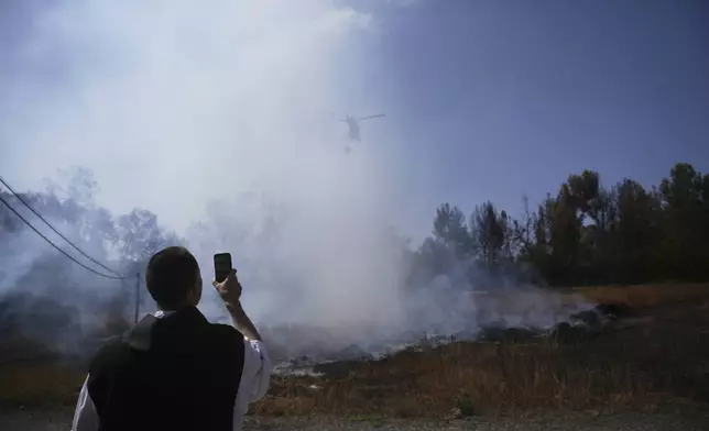 A Roman Catholic Trappist monk films an Israeli fire crew helicopter battling a wildfire outside his monastery in Latrun, Israel, outside of Jerusalem, Thursday, May 1, 2025. (AP Photo/Ohad Zwigenberg)