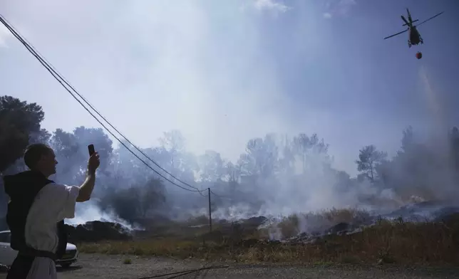 A Roman Catholic Trappist monk films an Israeli fire crew helicopter battling a wildfire outside his monastery in Latrun, Israel, outside of Jerusalem, Thursday, May 1, 2025. (AP Photo/Ohad Zwigenberg)