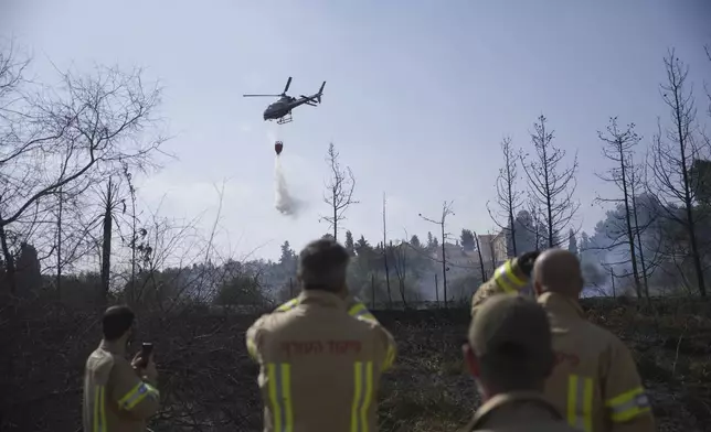 Israeli firefighters watch a helicopter drop water on a wildfire next to a monastery in Latrun, Israel, outside of Jerusalem, Thursday, May 1, 2025. (AP Photo/Ohad Zwigenberg)