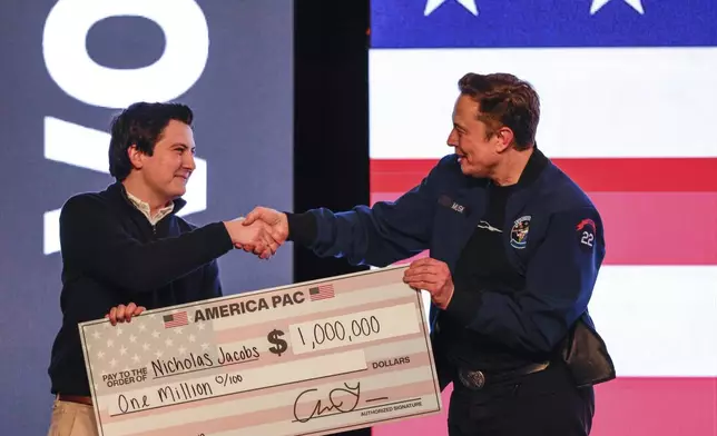 FILE - Elon Musk presents a check for $1 million dollars to a man during a town hall March 30, 2025, in Green Bay, Wis. (AP Photo/Jeffrey Phelps, File)