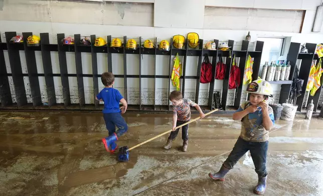 Children help clean up the fire station after flooding on Wednesday, May 14, 2025 in Westernport, Md. (AP Photo/Gene J. Puskar)