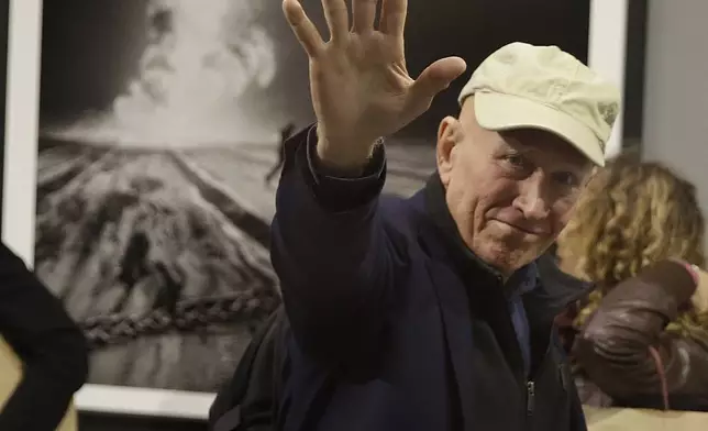 FILE - Photographer Sebastiao Salgado waves to photographers during the presentation of his exhibition, 'Kuwait: A Desert on Fire', at the Galleria Meravigli, in Milan, Italy, Oct. 20, 2017. Salgado, known for his long-term projects and images of nature and humanity, died at age 81, the Instituto Terra confirmed on Friday, May 23, 2025. (AP Photo/Luca Bruno, File)