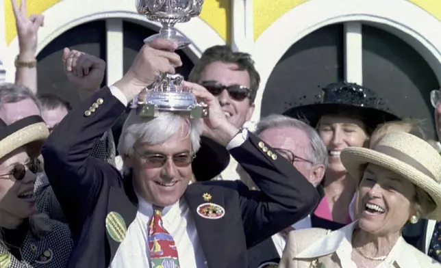 FILE - In this May 17, 1997, file photo, trainer Bob Baffert holds the Preakness Trophy atop his head as Silver Charm's owner Beverly Lewis looks on, at right, in the winner's circle at Pimlico Race Course in Baltimore. (AP Photo/Roberto Borea, File)