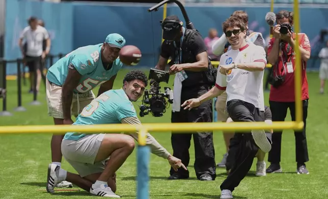 Ferrari driver Charles Leclerc of Monaco, right, kicks a ball as he tries out kicking football field goals with Miami Dolphins linebackers Jaelan Phillips (15) and Quinton Bell (56), during a joint event ahead of the Formula One Miami Grand Prix auto race, Thursday, May 1, 2025, in Miami Gardens, Fla. (AP Photo/Rebecca Blackwell)