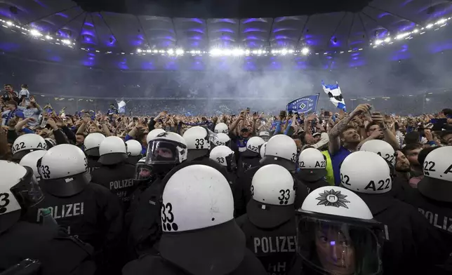 Police officers stand guard as Hamburg fans storm the pitch to celebrate promotion following a Bundesliga 2 soccer game between Hamburger SV and SSV Ulm 1846 in Hamburg, Germany, Saturday, May 10, 2025. (Christian Charisius/dpa via AP)