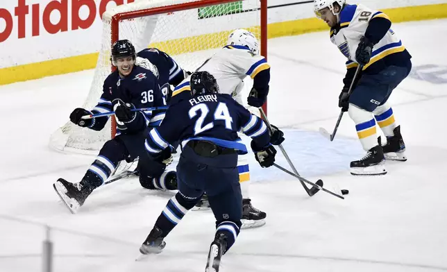 Winnipeg Jets' Morgan Barron (36) and Haydn Fleury (24) defend against St. Louis Blues' Cam Fowler (17) and Robert Thomas (18) in front of Jets goaltender Connor Hellebuyck, second from left, during the second period of Game 7 in an NHL hockey first-round playoff series in Winnipeg, Manitoba, Sunday, May 4, 2025. (Fred Greenslade/The Canadian Press via AP)