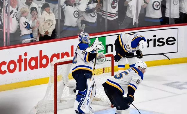 St. Louis Blues' goaltender Jordan Binnington (50), Colton Parayko (55) and Cam Fowler (17) react as the Winnipeg Jets celebrate their game-winning goal in the second overtime period of Game 7 in an NHL hockey first-round playoff series in Winnipeg, Manitoba, Sunday, May 4, 2025. (Fred Greenslade/The Canadian Press via AP)