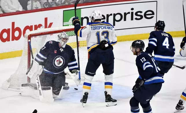 St. Louis Blues' Alexey Toropchenko (13) celebrates a goal by Radek Faksa (not shown) against Winnipeg Jets goaltender Connor Hellebuyck, left, during the second period of Game 7 in an NHL hockey first-round playoff series in Winnipeg, Manitoba, Sunday, May 4, 2025. (Fred Greenslade/The Canadian Press via AP)