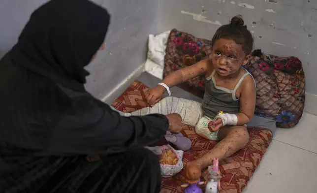 Raika Abu Sahloul, 40, cares for her 4-year-old niece, Layan, as she sits despondently among her dolls at Nasser hospital with second-degree burns on her face, foot, and stomach, caused a week earlier during an Israeli army strike on her home in Khan Younis that killed her pregnant mother and two siblings and buried her under the rubble, in Khan Younis, Gaza Strip, Sunday, May 4, 2025.(AP Photo/Abdel Kareem Hana)