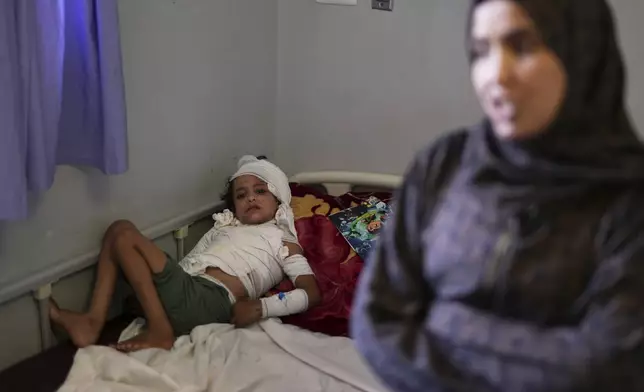 Iman Abu Shabab, 30, stands next to her 7-year-old son, Hamza, who lies in bed with third-degree burns caused when, frightened by an Israeli airstrike, he spilled a hot plate of rice and lentils on himself in the family's tent in southern Gaza last month, at Nasser hospital in Khan Younis, Gaza Strip, Sunday, May 4, 2025.(AP Photo/Abdel Kareem Hana)