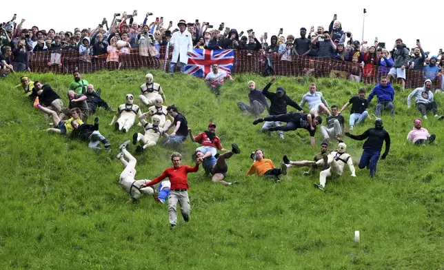 Participants compete in the men's downhill race category of the traditional annual Cheese Rolling contest at Cooper's Hill in Brockworth, Gloucestershire, England, Monday, May 26, 2025.(AP Photo/Anthony Upton)