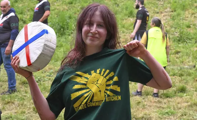 Ava Sender Logan shows the cheese roll after winning the women's downhill race category of the traditional annual Cheese Rolling contest at Cooper's Hill in Brockworth, Gloucestershire, England, Monday, May 26, 2025. (AP Photo/Anthony Upton)