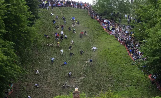 Participants compete in the men's downhill race category of the traditional annual Cheese Rolling contest at Cooper's Hill in Brockworth, Gloucestershire, England, Monday, May 26, 2025.(AP Photo/Anthony Upton)