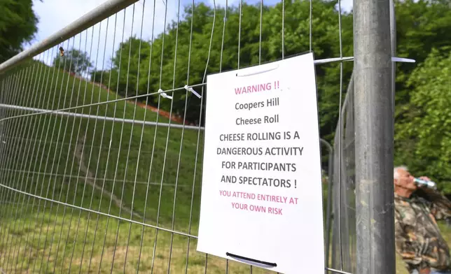 A signpost warns participants and spectators of the dangers of the traditional annual Cheese Rolling contest at Cooper's Hill in Brockworth, Gloucestershire, England, Monday, May 26, 2025.(AP Photo/Anthony Upton)