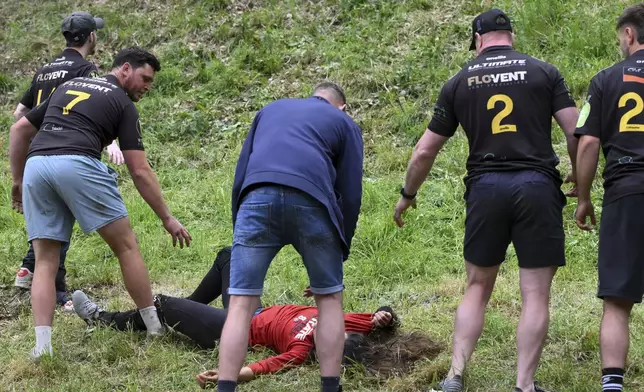 A participant rests after the women's downhill race of the traditional annual Cheese Rolling contest at Cooper's Hill in Brockworth, Gloucestershire, England, Monday, May 26, 2025.(AP Photo/Anthony Upton)