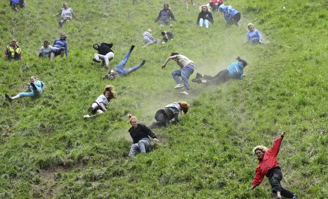 Participants compete in the women's downhill race category of the traditional annual Cheese Rolling contest at Cooper's Hill in Brockworth, Gloucestershire, England, Monday, May 26, 2025.(AP Photo/Anthony Upton)