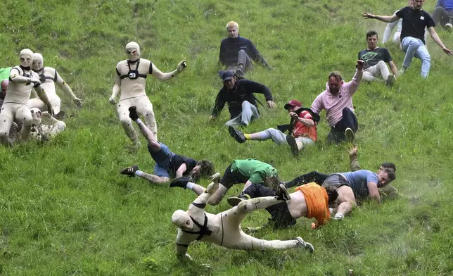 Participants, some dressed as a "crash test dummies" in a morph suits, compete in the men's downhill race category of the traditional annual Cheese Rolling contest at Cooper's Hill in Brockworth, Gloucestershire, England, Monday, May 26, 2025.(AP Photo/Anthony Upton)