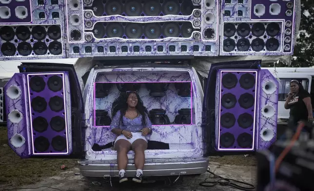 A woman sits on speakers playing music during a Red Devils bus exhibition in La Chorrera, Panama, Sunday, June 30, 2024. The Red Devils are former U.S. school buses once used in the Panama Canal Zone and later as public transport, now adapted for private and cultural use. (AP Photo/Matias Delacroix)
