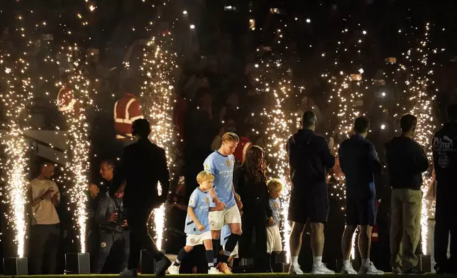 Manchester City's Kevin De Bruyne accompanied by his family walks on the pitch after his final home game during the English Premier League soccer match between Manchester City and Bournemouth at the Etihad stadium in Manchester, England, Tuesday, May 20, 2025. (AP Photo/Dave Thompson)