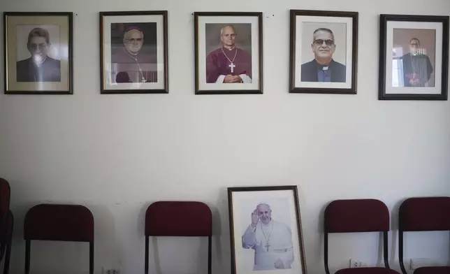 A photo of newly elected Pope Leo XIV, center, hangs among portraits of bishops of the Diocese of Chiclayo, above one of the late Pope Francis, at the bishop's residence and office in Chiclayo, Peru, Friday, May 9, 2025. (AP Photo/Guadalupe Pardo)