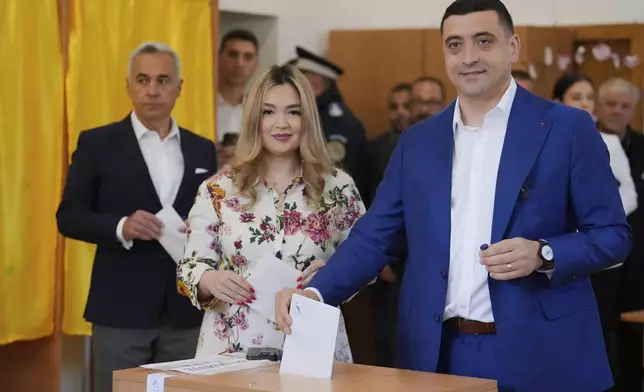Presidential candidate George Simion casts his vote next to his wife Ilinca in the second round of the country's presidential election redo in Mogosoaia, Romania, Sunday, May 18, 2025. (AP Photo/Vadim Ghirda)