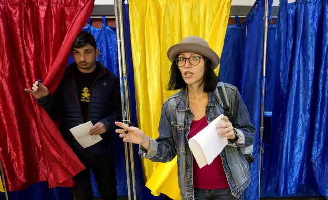 People exit voting cabins with the colours of the Romanian flag as curtains, before casting their vote, in the second round of the country's presidential election redo in Bucharest, Romania, Sunday, May 18, 2025. (AP Photo/Andreea Alexandru)