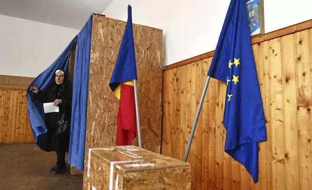 A woman exits a voting cabin before casting her ballot in the second round of the country's presidential election redo in Persani, Romania, Sunday, May 18, 2025. (AP Photo/Eduard Vinatoru)
