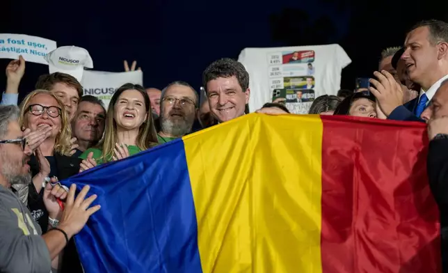 Presidential candidate Nicusor Dan, center, poses behind a Romanian flag after polls closed for the second round of the country's presidential election redo in Bucharest, Romania, Sunday, May 18, 2025. (AP Photo/Andreea Alexandru)