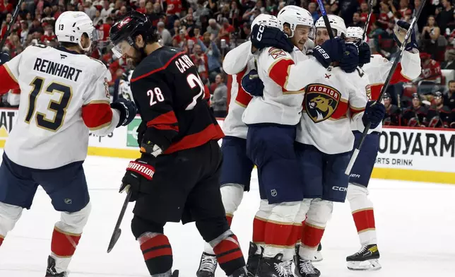 Florida Panthers' Carter Verhaeghe, right, celebrates his goal with teammate Aleksander Barkov (16), center with Sam Reinhart (13) and Carolina Hurricanes' William Carrier (28) nearby during the third period of Game 5 of the NHL hockey Stanley Cup Eastern Conference finals in Raleigh, N.C., Wednesday, May 28, 2025. (AP Photo/Karl DeBlaker)