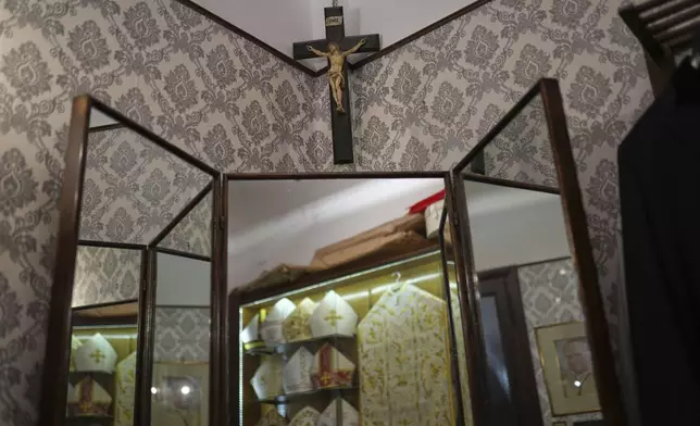 A crucifix hangs over a mirror reflecting ecclesiastic clothes inside the dressing room at the Gammarelli tailor shop in Rome, Wednesday, April 30, 2025. (AP Photo/Francisco Seco)