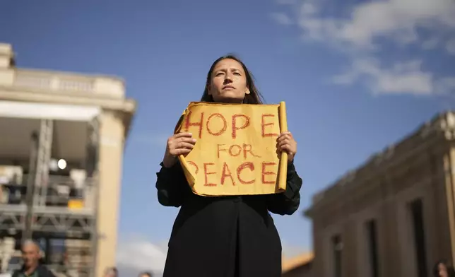 A woman holds up a sign for peace in St Peter's Square during the cardinals' conclave to elect a new pope, at the Vatican, Wednesday, May 7, 2025. (AP Photo/Francisco Seco)