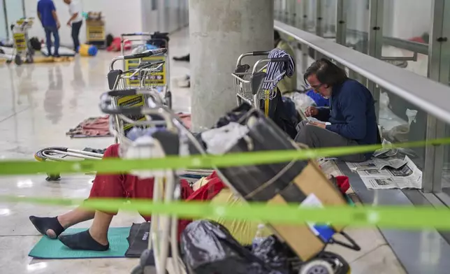 A person eats sitting on the floor of Terminal 4 at Adolfo Suarez-Madrid Barajas Airport in Madrid, Spain, Thursday, May 15, 2025. (AP Photo/Manu Fernandez)