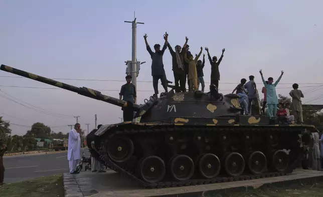 Pakistanis flash victory signs as they celebrate on top of a model of a tank following India and Pakistan have reached a ceasefire deal, during a demonstration, in Multan, Pakistan, Saturday, May 10, 2025. (AP Photo/Asim Tanveer)
