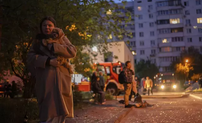 A woman carries her dog as she walks on a street with pieces of broken glass at the site of a residential building that was damaged after a Russian attack in Kyiv, Ukraine, Saturday, May 24, 2025. (AP Photo/Alex Babenko)