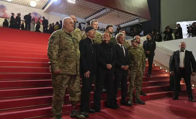 The Edge, from second left, Bono and Sean Penn pose with military personnel for photographers upon arrival at the premiere of the film 'Bono: Stories of Surrender' at the 78th international film festival, Cannes, southern France, Friday, May 16, 2025. (AP Photo/Natacha Pisarenko)