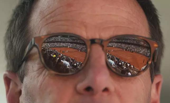 The court Simonne-Mathieu is reflected in the sunglasses of Jeff Amsel as he watches the first round match of the French Tennis Open between Taylor Fritz of the United States, and Germany's Daniel Altmaier, at the Roland-Garros stadium, in Paris, Monday, May 26, 2025. (AP Photo/Lindsey Wasson)