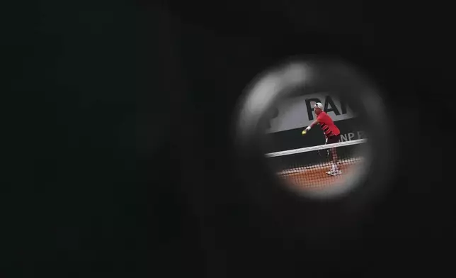 Denmark's Holger Rune is seen through a hole in a tarp on a fence as he prepares to serve a ball to Spain's Roberto Bautista Agut, during their first round match of the French Tennis Open, at the Roland-Garros stadium, in Paris, Monday, May 26, 2025. (AP Photo/Lindsey Wasson)