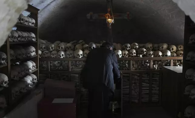 Father Serafeim lights a candle inside an ossuary where the shelves are full of the skulls of the deceased monks of the Simonopetra, or Simonos Petra Monastery, home of the all-male autonomous community of Agion Oros, or Holy Mountain, on the peninsula of Mount Athos in northern Greece, Monday, April 14, 2025. (AP Photo/Thanassis Stavrakis)