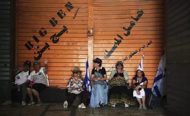 Israelis sit next to a closed Palestinian shop during a march marking Jerusalem Day, an Israeli holiday celebrating the capture of east Jerusalem in the 1967 Mideast war, in Jerusalem's Old City, Monday, May 26, 2025. (AP Photo/Ohad Zwigenberg)