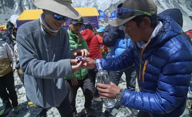 A sherpa hands vodka, that was earlier offered to the Gods, to a climber after a ritual for a safe climb at Everest Base Camp before beginning his ascent to the summit of Mount Everest in Nepal, April 24, 2025. (AP Photo/Pasang Rinzee Sherpa)