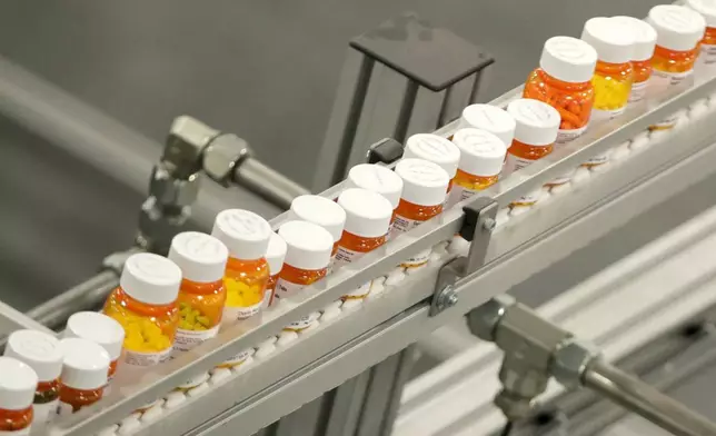 FILE- Bottles of medicine ride on a belt at a mail-in pharmacy warehouse in Florence, N.J., July 10, 2018. President Donald Trump’s plan to change the pricing model for some medications is facing fierce criticism from the pharmaceutical industry before he’s even signed an executive order he says will lower the costs of drugs. (AP Photo/Julio Cortez, File)