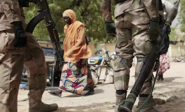 FILE - A woman walks past Nigerian soldiers at a checkpoint in Gwoza, northeast, Nigeria, April 8, 2015. (AP Photo/Lekan Oyekanmi, File)