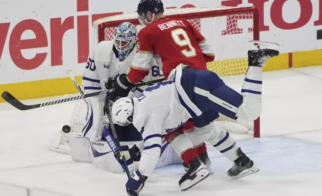 Toronto Maple Leafs center John Tavares, center, falls to the ice as goaltender Joseph Woll (60) defends the goal against Florida Panthers center Sam Bennett (9) during the third period in Game 6 of a second-round NHL hockey playoff series, Friday, May 16, 2025, in Sunrise, Fla. (AP Photo/Lynne Sladky)