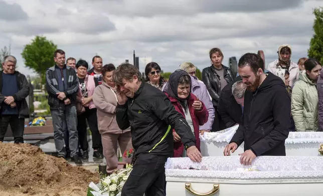 A father, left, mourns his children Tamara Martyniuk, 8, Stanislav Martyniuk, 12, and Roman Martyniuk, 17, killed in a Russian strike on Sunday, during farewell ceremony in Korostyshiv, Zhytomyr region, Ukraine, Wednesday, May 28, 2025. (AP Photo/Evgeniy Maloletka)