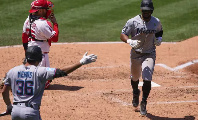 Miami Marlins' Otto Lopez, right, is congratulated by Matt Mervis, left, after scoring on a single by Connor Norby as Los Angeles Angels catcher Travis d'Arnaud stands by during the fourth inning of a baseball game Sunday, May 25, 2025, in Anaheim, Calif. (AP Photo/Mark J. Terrill)