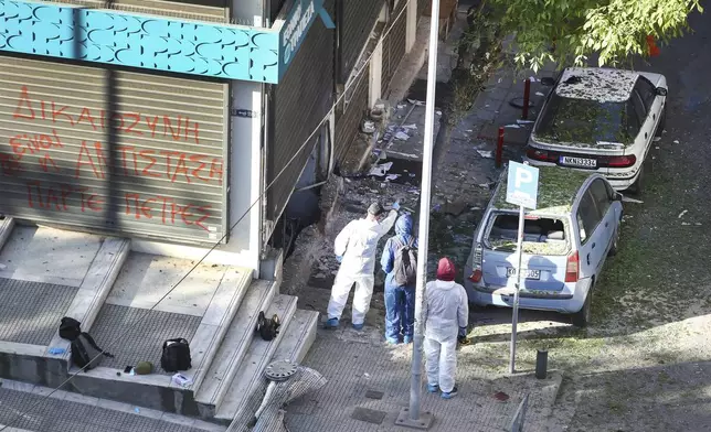 Greek police forensic experts search the area where a 38-year-old woman was killed early Saturday when a bomb she was carrying exploded in her hands outside a bank branch, local police said, in Thessaloniki, northern Greece, May 3, 2025. On the fence of the bank branch reads : "Justice is to resist. Take stones". (AP Photo/Giannis Papanikos)