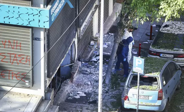 Greek police forensic experts search the area where a 38-year-old woman was killed early Saturday when a bomb she was carrying exploded in her hands outside a bank branch, local police said, in Thessaloniki, northern Greece, May 3, 2025. (AP Photo/Giannis Papanikos)