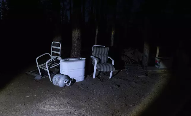 A flashlight from Mandy Bryant's shines on chairs propped up by trees at a homeless encampment in Deschutes National Forest Wednesday, April 30, 2025 near Bend, Ore. (AP Photo/Jenny Kane)
