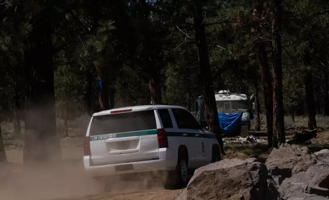 A U.S. Forest Service vehicle drives down a dirt road past newly placed rock barrier towards a trailer at a homeless encampment in Deschutes National Forest, Thursday, May 1, 2025, near Bend, Ore. (AP Photo/Jenny Kane)