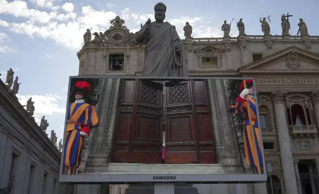 A giant screen in St Peter's Basilica shows a Vatican official closing the door to the Sistine Chapel after calling out "extra omnes", Latin for "all out", during the cardinals' conclave to elect a new pope, at the Vatican, Wednesday, May 7, 2025. (AP Photo/Alessandra Tarantino)